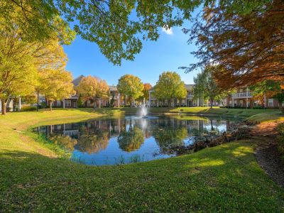 Shaded walking paths framing a central community pond with a water fountain and vibrant seasonal trees at The Westbury apartments near Germantown.