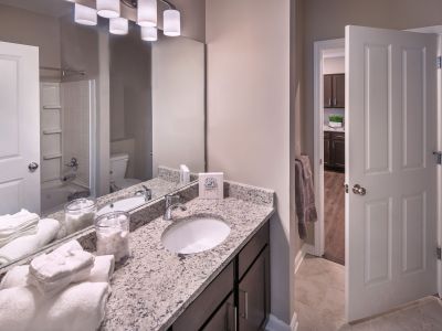 Upgraded apartment bathroom showing a granite-topped double vanity, wide mirror, and bright lighting features at The Westbury apartments near Germantown.