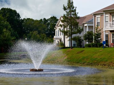 Scenic outdoor water fountain spraying in a community pond with grassy banks and multi-story residential buildings at The Westbury apartments near Germantown.
