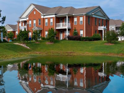 Exterior of a multi-story red brick residential building perfectly reflecting across a calm community pond at The Westbury apartments near Germantown.